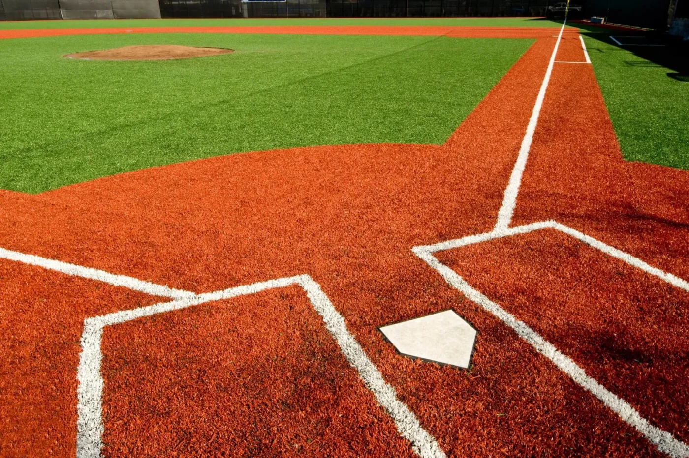 A baseball field with low-maintenance artificial grass is shown, nestled in Paradise Valley, AZ. The home plate and a portion of the infield feature vibrant red and green turf. Crisp white lines mark the field boundaries, while the pitcher's mound stands proud in the background.