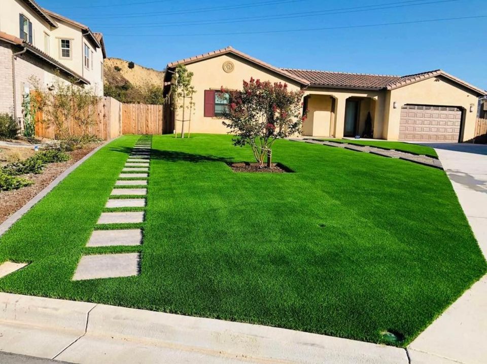 A suburban house with a well-maintained front yard featuring vivid artificial grass. There is a winding stone path leading to the home's entrance, and the house has a red-tile roof with a two-car garage on the right, making this Paradise Valley lawn picture-perfect.